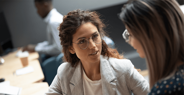Confident businesswoman wearing glasses discussing project with colleague close up in office
